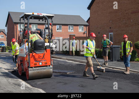 Squadra che posa Tarmac, bitmac, aspahlt e utilizzando rulli stradali in un nuovo sviluppo di case in St Anne's in mare. Tarmacadam, propriamente chiamato macadam bituminoso o 'Bitmac' per brevità, è spesso pensato per essere il metodo più economico di superficie di un viale o di un piazzale, macadam è un processo di legare insieme aggregati più piccoli, come pionierizzato dal leggendario John MacAdam nel 19 ° secolo. Lytham, Blackpool, Regno Unito Foto Stock