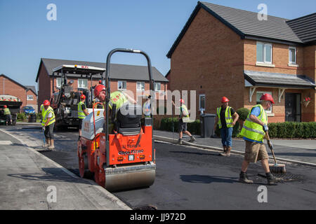 Squadra che posa Tarmac, bitmac, aspahlt e utilizzando rulli stradali in un nuovo sviluppo di case in St Anne's in mare. Tarmacadam, propriamente chiamato macadam bituminoso o 'Bitmac' per brevità, è spesso pensato per essere il metodo più economico di superficie di un viale o di un piazzale, macadam è un processo di legare insieme aggregati più piccoli, come pionierizzato dal leggendario John MacAdam nel 19 ° secolo. Lytham, Blackpool, Regno Unito Foto Stock