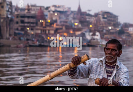 Un rematore righe una barca per turisti sul fiume Gange a Varanasi, Uttar Pradesh, India con la cremazione incendi a Manikarnika Ghat in backgrou Foto Stock