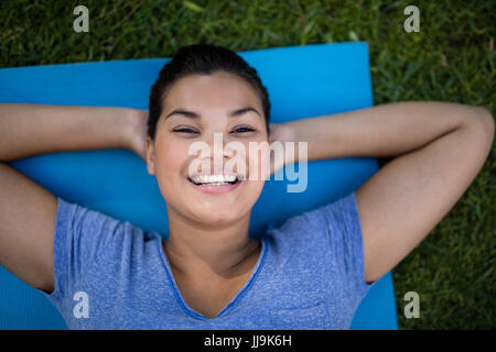 Angolo alto ritratto di trainer sorridente giacente sul tappeto di esercizio in posizione di parcheggio Foto Stock