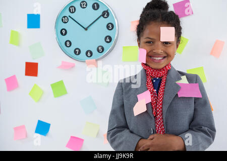 Imprenditrice sorridente con note adesive bloccato sulla tuta e permanente di testa contro la parete Foto Stock
