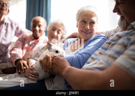 Senior donna coniglio di contenimento mentre è seduto con gli amici sul divano di casa di cura Foto Stock