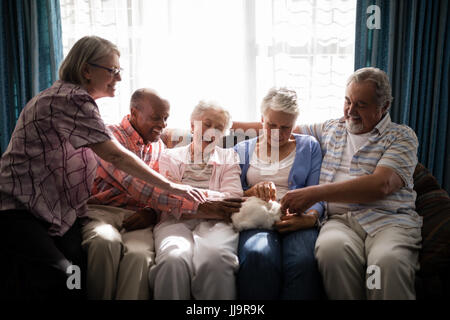 Multi-etnico senior amici a giocare con il coniglio comodamente seduti sul divano di casa di cura Foto Stock