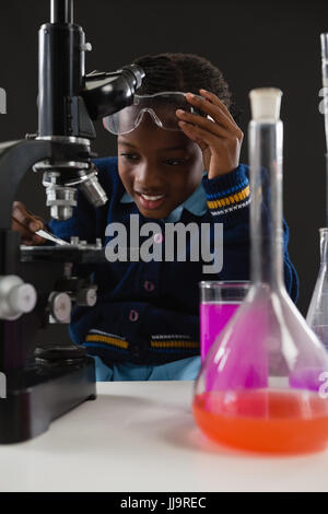 Attento schoolgirl usando microscopio su sfondo nero Foto Stock