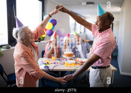 Coppia senior rendendo il telaio contro gli amici tenendo le mani mentre godendo nella festa di compleanno Foto Stock
