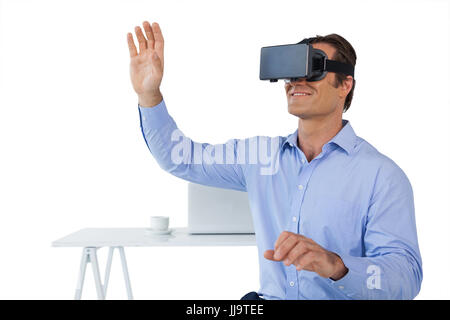 Imprenditore sorridente con le braccia sollevate utilizzando occhiali vr mentre seduto contro uno sfondo bianco Foto Stock