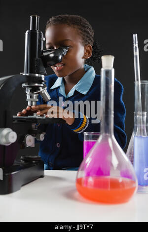 Attento schoolgirl usando microscopio su sfondo nero Foto Stock