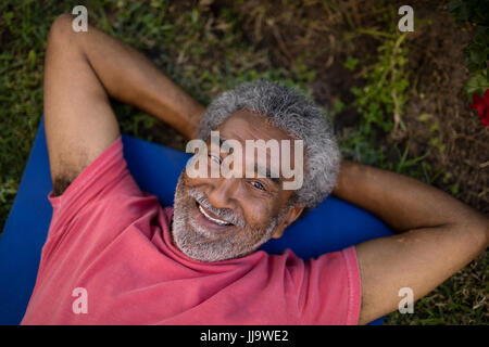 Angolo alto ritratto di sorridente maschio senior in appoggio mentre giaceva sul tappeto di esercizio in posizione di parcheggio Foto Stock