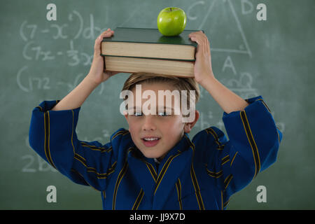 Ritratto di scolaro holding pila di libri con apple contro la lavagna Foto Stock