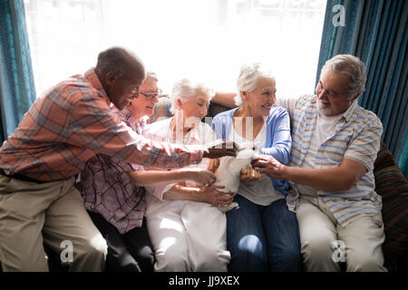 Sorridente senior amici a giocare con il coniglio comodamente seduti sul divano di casa di cura Foto Stock