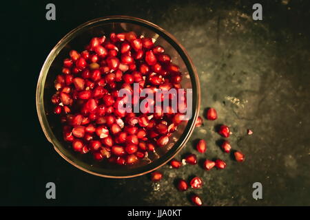 Fresche, sbucciato e succosa e i semi di melograno in vaso di vetro su uno sfondo scuro. Foto Stock