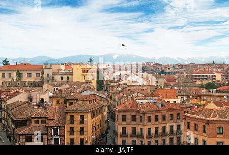 Vista aerea della vecchia città spagnola di Segovia in primavera con cime innevate a sfondo e una cicogna volando sopra la città di Segovia, Spagna Foto Stock