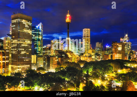 Panorama della città di Sydney alti torri illuminate al tramonto in piedi su alberi verdi della centrale di Hyde Park. Foto Stock