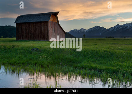 Un vecchio fienile lungo il Mormon fila in piedi al di sopra di un flusso che riflette un tramonto colorato in Jackson Hole. Il Parco Nazionale del Grand Teton, Wyoming Foto Stock