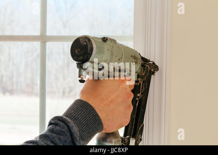 Carpenter mediante pistola sparachiodi per cornici su windows, framing trim, Foto Stock