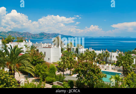Ville bianche con palme in Profesorler Sitesi a Amos Bay nel Mare Egeo con isole montagnose e nuvole a sfondo sulla giornata di sole Foto Stock