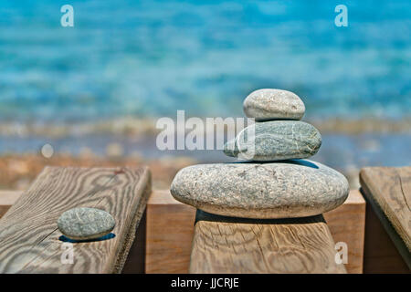 Tre ciottoli grigio sovrapposti su tavole di legno con il mare blu acqua a sfondo, Marmaris, Turchia Foto Stock