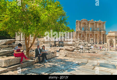 Izmir, Turchia - 14 maggio, 2015: tre turisti che si siedono sulle panchine di pietra in appoggio sotto il blooming melograno sul caldo giorno di primavera nel patrimonio mondiale di UNESCO si Foto Stock