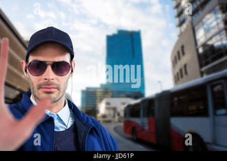 Fiducioso security officer che mostra il gesto di arresto contro cityscape contro il cielo nuvoloso Foto Stock