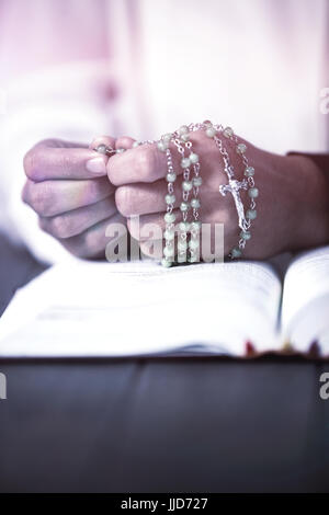 Pregando le mani della donna con il rosario e la bibbia sulla scrivania in legno Foto Stock