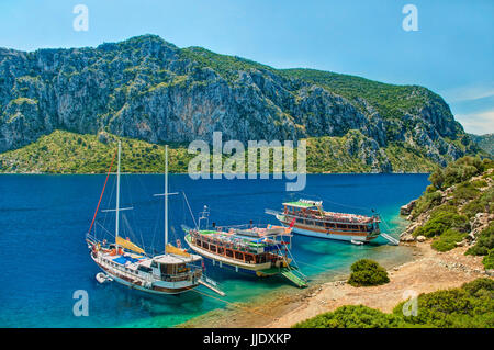 Tre imbarcazioni turistiche ormeggiato a Camellia island beach con isola rocciosa a sfondo contro il cielo blu e chiaro sulla giornata di sole, Hisaronu Bay, Mar Egeo, Tur Foto Stock