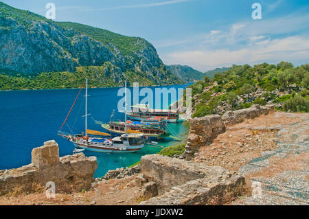 Vista della montagna con tre barche in mare Egeo a Camellia isola dalle rovine di epoca medievale chiesa bizantina, Marmaris, Turchia Foto Stock