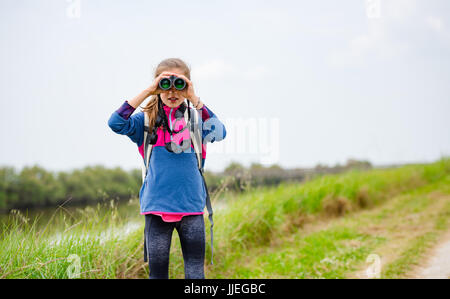 Ragazza giovane guardando attraverso il binocolo sulla riva del fiume Foto Stock