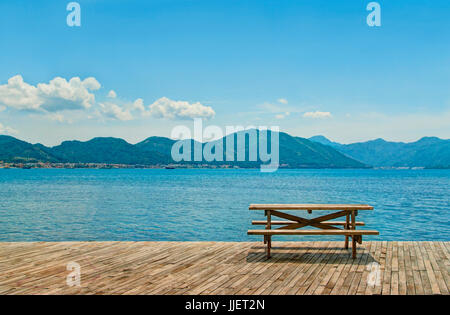 Tavolo in legno e due panche per picnic in piedi sul pavimento in legno dal mare sulla giornata soleggiata affacciata verde isole montagnose vicino a Marmaris, Turchia Foto Stock