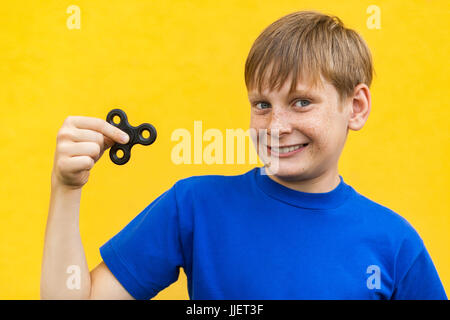 Giovane bella felice ragazzo con lentiggini blu t-shirt holding agitano: spinner su sfondo giallo. Foto Stock