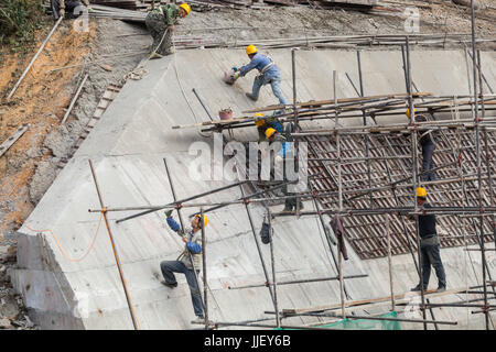 I lavoratori salgono su impalcature e costruiscono una spessa parete di cemento alla foce di una grande diga di deviazione (box) nel sito della diga n. 6 sul fiume Nam Ou, Laos. Foto Stock