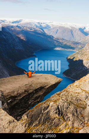Uomo seduto sulla roccia Trolltunga meditando, Odda, Hordaland, Norvegia Foto Stock
