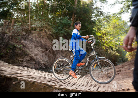Un ragazzo corse la sua bicicletta oltre il bamboo ponte sopra il flusso tributario al fiume Nam Ou al di fuori di Ban Huay Phouk, Laos. Foto Stock