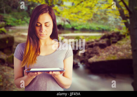 Bruna giovane azienda digitale compressa contro rapids che scorre lungo la foresta Foto Stock