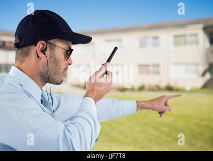 Digital composito della guardia di sicurezza tenendo walkie talkie e gesticolando mentre si sta in piedi sul campo Foto Stock