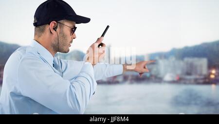 Digital composito della guardia di sicurezza con walkie talkie puntato contro lo skyline di sfocato Foto Stock