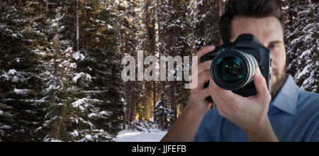 Fotografo maschio fotografando attraverso la telecamera contro la strada ghiacciata tra filari di alberi innevati Foto Stock