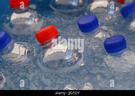 Bottiglie in plastica PET di freddo ancora e scintillante di bere acqua minerale con blu e cappucci rossi galleggiante e raffreddare in acqua e ghiaccio sul mercato al dettaglio di Foto Stock