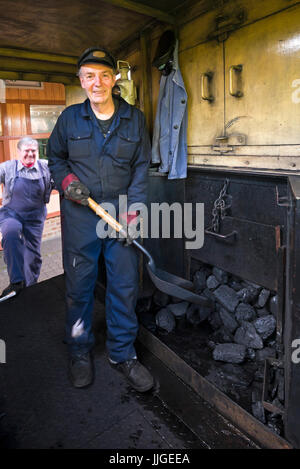 Ritratto verticale di un vigile del fuoco in piedi sulla pedana di una locomotiva a vapore. Foto Stock