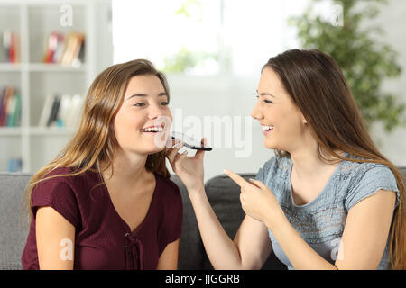 Due amici in ascolto di messaggi audio su uno smart phone seduto su un divano nel soggiorno di casa Foto Stock