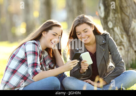 Due felici gli amici a guardare i contenuti multimediali nella loro smart phone seduta sul prato di un parco Foto Stock