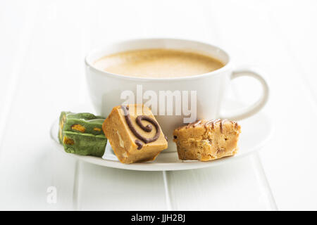 Colorate caramelle di caramello e la tazza di caffè sul tavolo bianco. Foto Stock