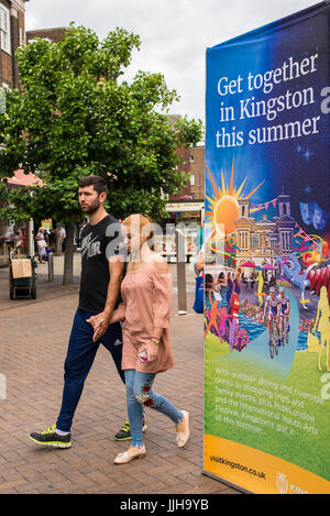 Giovane camminare al fianco di un grande cartellone su Clarence Street, la principale strada pedonale dello shopping a Kingston Upon Thames promuovere manifestazioni estive Foto Stock