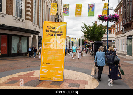 Le persone camminare al fianco di un grande tabellone giallo su Clarence Street, la principale strada pedonale dello shopping a Kingston Upon Thames mostrare le summe Foto Stock