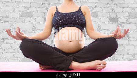 Donna incinta metà sezione meditando bianco contro un muro di mattoni Foto Stock