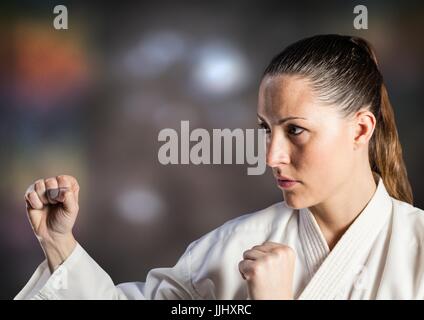 Donna in tuta di karate in posa contro sfocato sfondo marrone Foto Stock