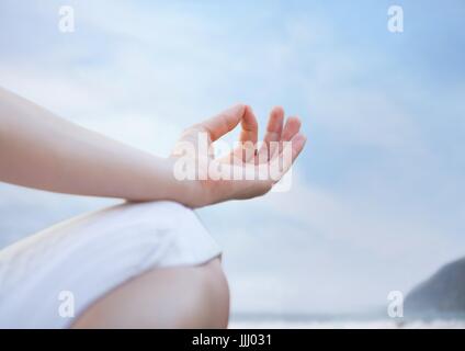 La mano e il ginocchio della donna meditando contro sfocata beach Foto Stock