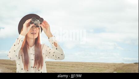 Donna che guarda attraverso il binocolo contro lo sfondo del paesaggio Foto Stock