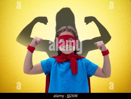 Happy girl vestirsi come una superwoman davanti a pugni disegnare sulla parete gialla Foto Stock