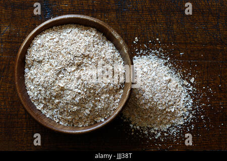 Crusca di frumento in legno scuro ciotola isolato in legno marrone scuro dal di sopra. Eventuali fuoriuscite di crusca di frumento. Foto Stock