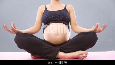 Donna incinta metà sezione meditando contro il muro grigio Foto Stock
